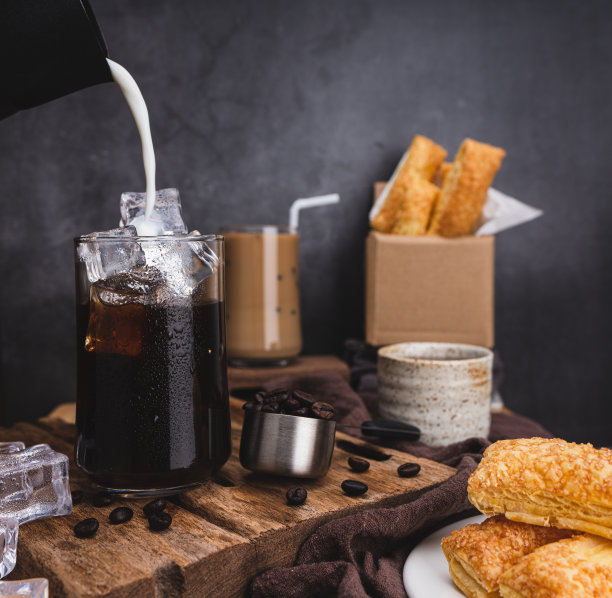 把用来做拿铁咖啡的牛奶倒入加冰的透明玻璃杯中。以及烤咖啡豆和木质脆皮派，黑色背景的工作室照片图片下载