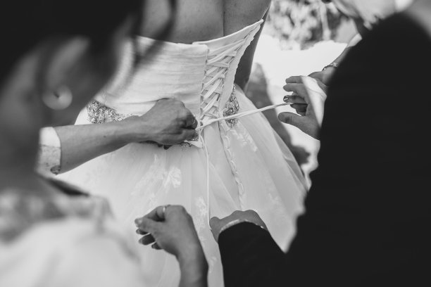 在婚礼当天，女性的手收紧新娘的胸衣的灰度特写图片下载