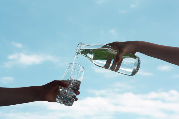 在天空背景下，新鲜干净的饮用水从瓶子中倒入玻璃中图片下载