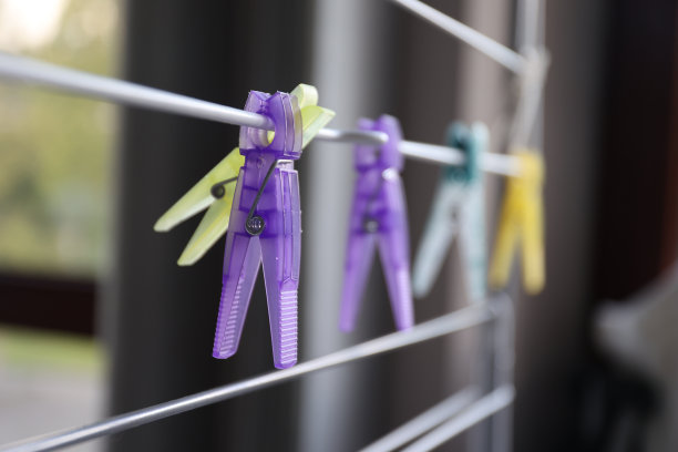 一个紫色的洗衣针挂在洗衣架上的特写肖像，旁边是其他彩色的洗衣夹或笔。它们被用来在室内或室外的架子上悬挂和晾晒衣服。图片下载