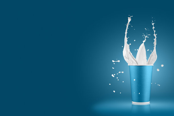 彩色背景上溅着牛奶的纸杯。有白色牛奶飞溅的一次性杯子。图片下载