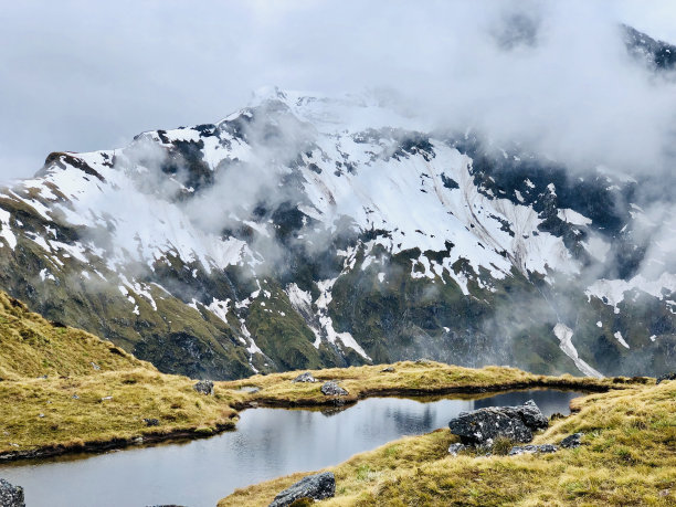 被雪和雾覆盖的山包围的小溪的特写镜头图片下载