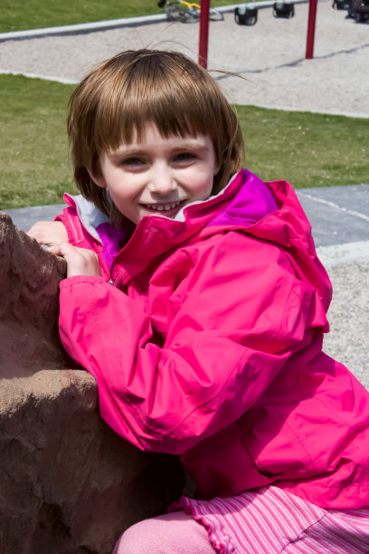 年轻的女孩穿着粉红色的外套和衣服，靠在操场上的设备图片下载