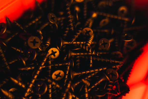 橙色灯光下，红色容器中有许多黑色自攻螺钉，特写图片下载