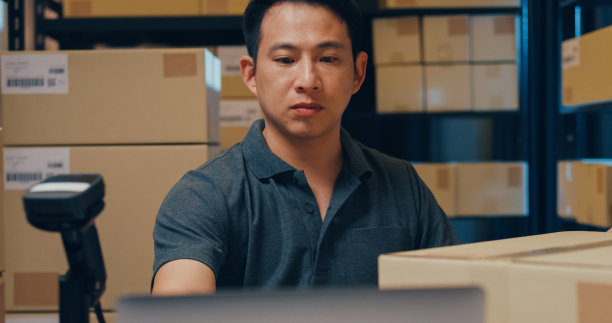 近距离的亚洲商人使用条形码机器扫描纸盒中的客户数据，并在笔记本电脑上键入注册在线信息订单明细，以便在仓库快递。图片下载