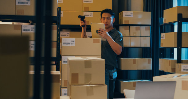 亚洲商人使用条形码扫描器扫描货架上的纸盒，把数据放在数字平板上，切割库存在线数据信息明细，以便在仓库快递。图片下载