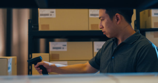 亚洲商人使用条形码扫描器扫描货架上的纸盒，把数据放在数字平板上，切割库存在线数据信息明细，以便在仓库快递。图片下载