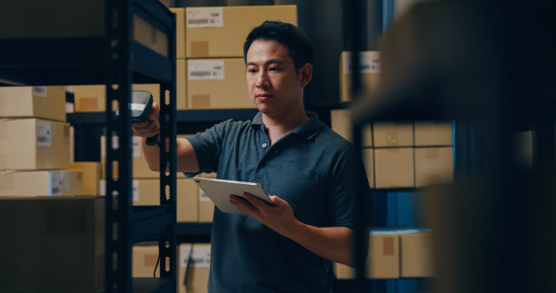 亚洲商人使用条形码扫描器扫描货架上的纸盒，把数据放在数字平板上，切割库存在线数据信息明细，以便在仓库快递。图片下载