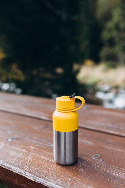 野外的树桌上放着一个黄色的真空套筒。林地步道上的远足装备。户外旅游概念图片下载