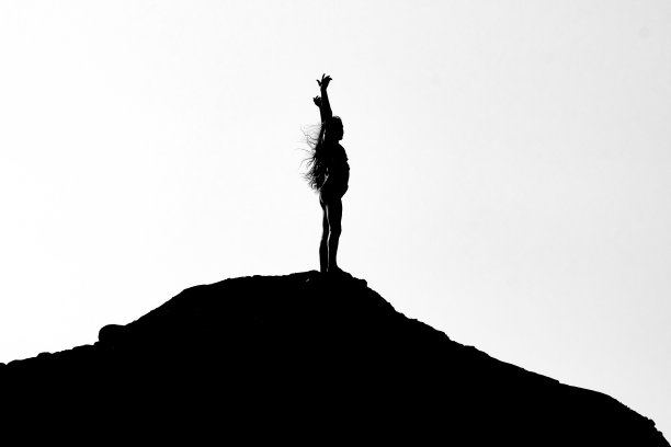 一个女孩站在岩石上，双手高举的灰色剪影图片下载