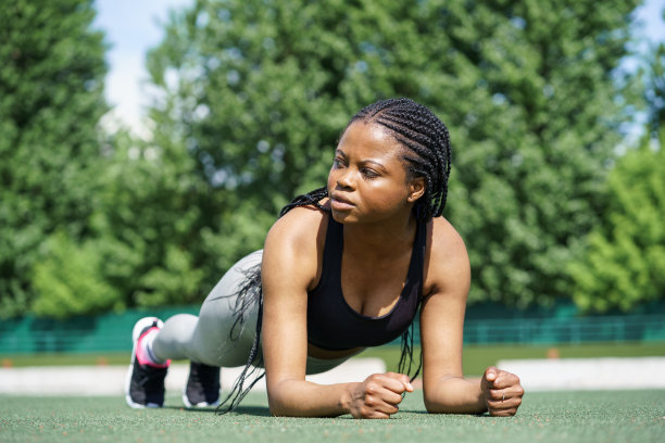 坚决的黑人妇女在城市体育场的绿色草皮地板上做平板支撑运动图片下载
