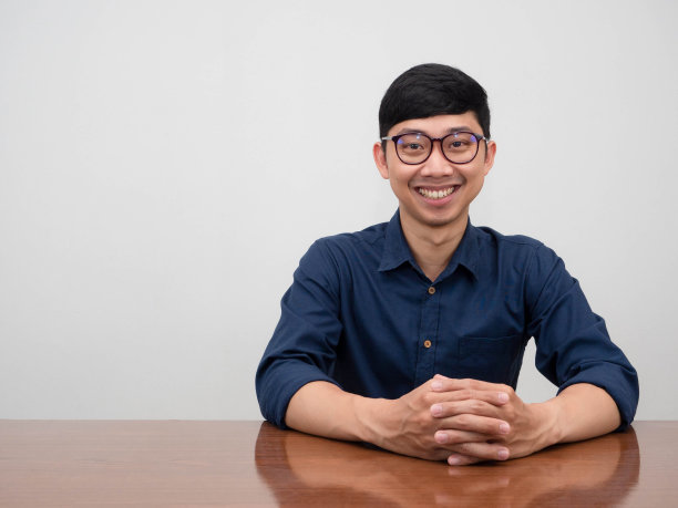 英俊的亚洲商人戴着眼镜坐在桌子前开心的微笑看着你图片下载