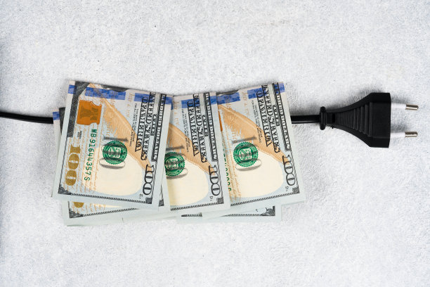 电缆上有黑色插头和许多100美元的钞票。全球电力价格上涨。高能源成本，世界能源和电力工业危机概念图片下载