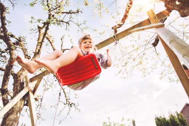 快乐的小女孩在家里的花园荡秋千。阳光灿烂的日子里，微笑积极健康的孩子在荡秋千。学龄前女孩又笑又哭。积极的休闲和户外活动。图片下载