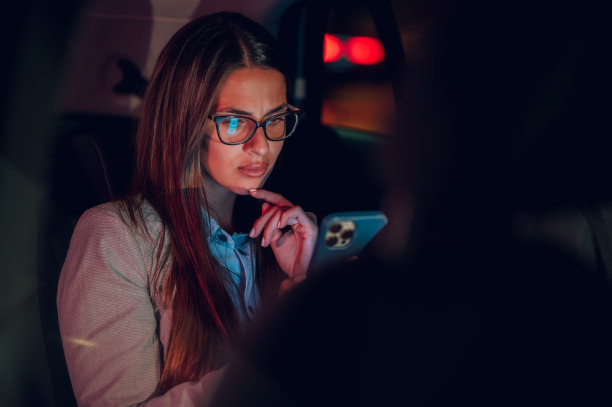 商务女性在晚上坐在汽车后座上使用智能手机图片下载