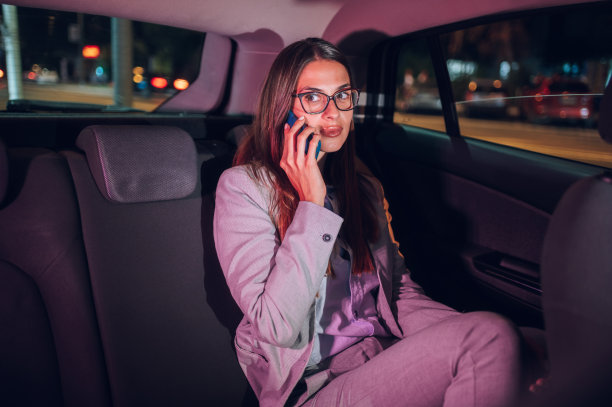 商务女性在晚上坐在汽车后座上使用智能手机图片下载