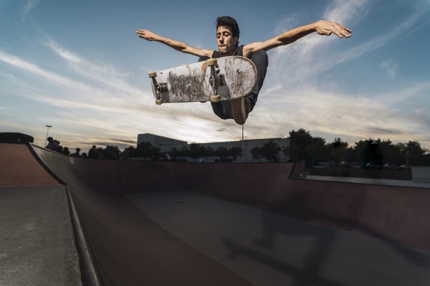 低角度拍摄的白人运动员男性在一个黑色的服装正在用滑板翻转魔术图片下载