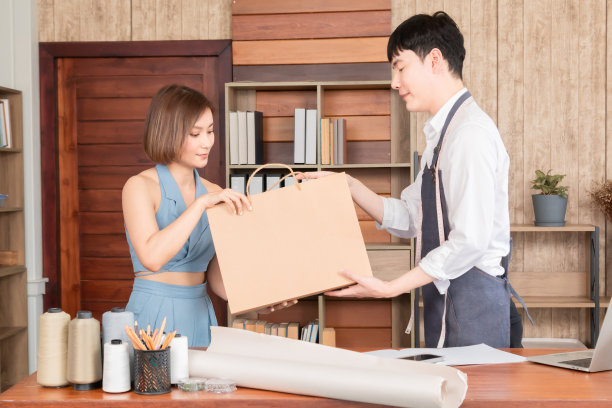 年轻的亚洲销售人员将购买的商品和衣服的购物袋给女性顾客，美丽的女性在定制服装店购买衣服，用信用卡支付。图片下载