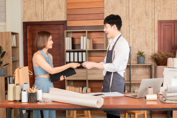 亚洲女性在定制服装店购买服装和使用信用卡支付的选择重点。年轻的销售人员把购买的商品和衣服的购物袋给女顾客。图片下载