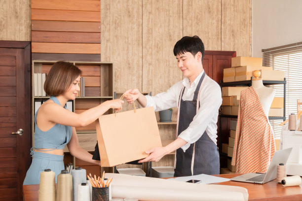 年轻的亚洲销售人员将购买的商品和衣服的购物袋给女性顾客，美丽的女性在定制服装店购买衣服，用信用卡支付。图片下载