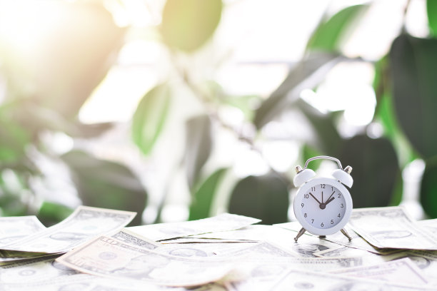 白色闹钟放在美国现金美元钱上面图片下载