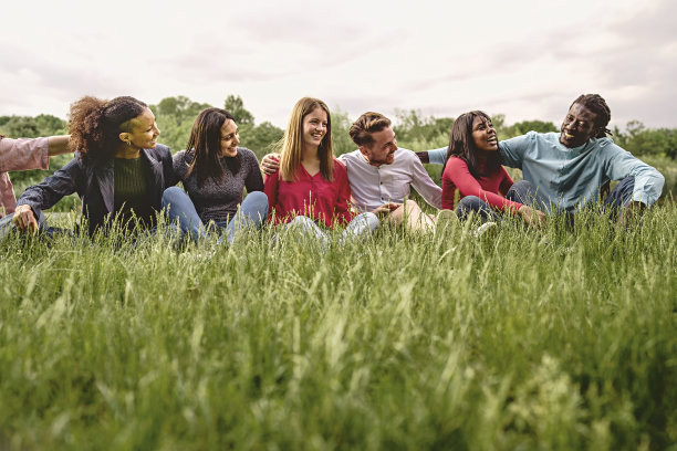 多民族大学生抱在一起，在草地上休息，微笑着，一起玩耍图片下载
