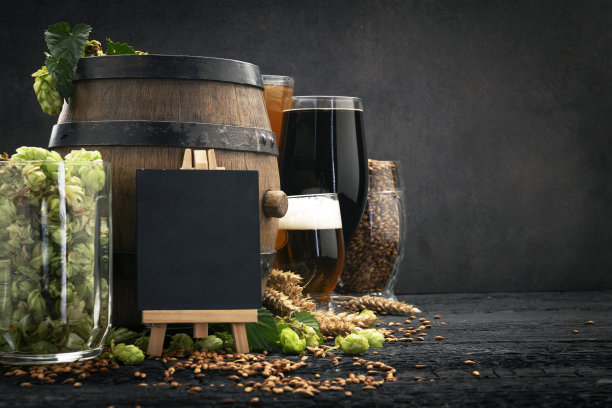 啤酒杯与绿色啤酒花和小麦在木制黑色背景图片下载