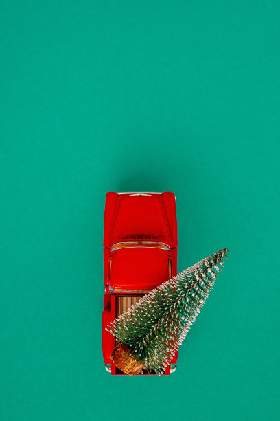 迷你红色汽车在后面带着一棵圣诞树在简单的绿色海蓝宝石背景，俯视图。节省空间。概念，喜庆圣诞心情，送礼物。这一趋势。图片下载