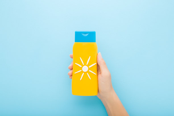 年轻的成年女性手拿黄色的防晒霜管在浅蓝色的背景。柔和的颜色。由白色奶油创建的太阳形状。夏天注意身体皮肤的保护。特写镜头。自顶向下视图。图片下载
