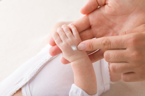 年轻的成年母亲在新生儿手上涂抹白色保湿霜。关心宝宝干净柔软的身体皮肤。特写镜头。图片下载