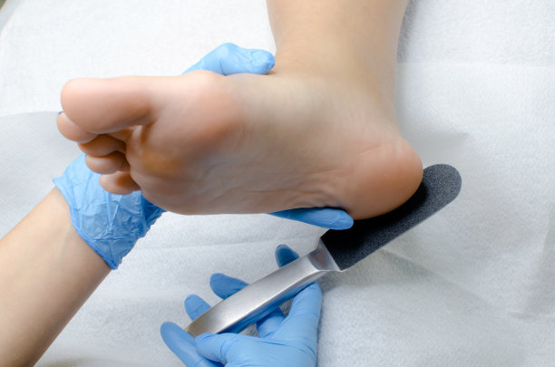 戴着蓝色手套的足疗师在美容院进行专业的医疗足疗。脚部治疗用特殊磨丝器近距离擦拭鞋跟图片下载