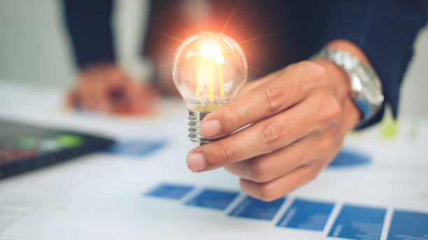 ฺBusinessman using a pen from financial statistics, holding a light bulb, with ideas, with innovation and creativity.图片下载