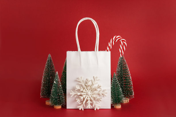 圣诞白纸购物袋与棒棒糖，雪花和圣诞树在一个红色的背景图片下载