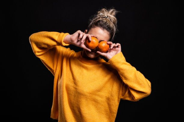 漂亮的照片，一个年轻的金发女孩在橙色毛衣摆姿势与小柑橘水果图片下载