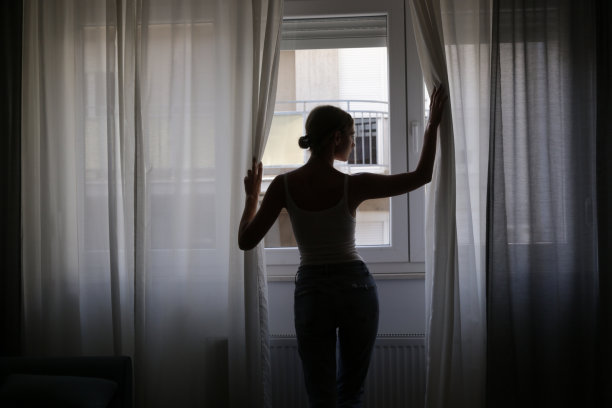公寓里女人揭开窗帘的剪影图片下载