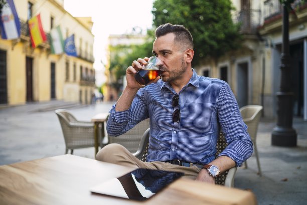 穿着正装的年轻男性坐在户外咖啡馆里喝冷饮图片下载