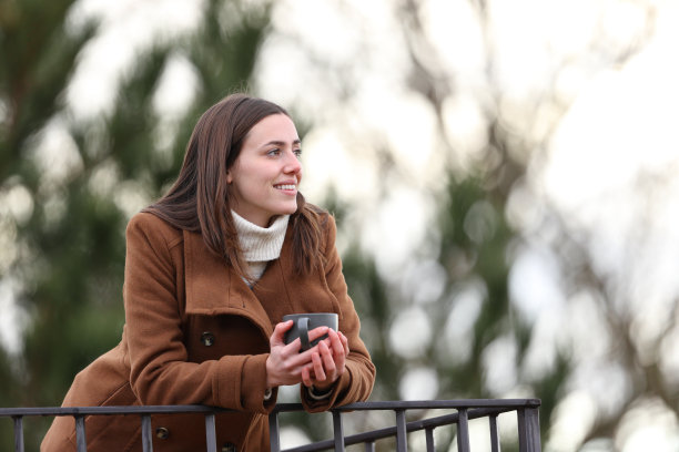 冬天阳台上拿着咖啡杯的快乐女人图片下载