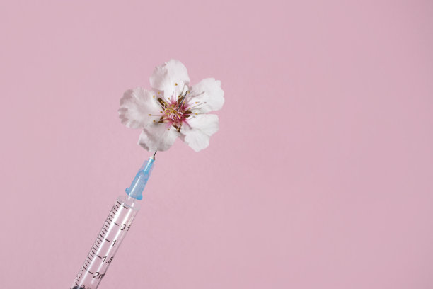 粉色背景上的天然粉色花朵和注射注射器。从上面看。整容手术的概念。图片下载