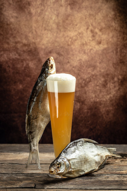 将啤酒倒入有浓厚泡沫的高脚杯中，在木制背景上放鱼干。啤酒啤酒厂的概念。啤酒干的零食。啤酒的背景图片下载