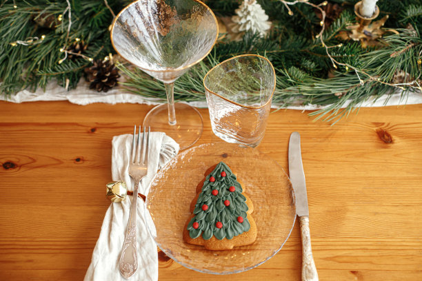 时尚的圣诞餐桌摆设。圣诞树饼干放在盘子里，亚麻餐巾和铃铛，古董餐具，葡萄酒杯，杉树树枝金色的灯，蜡烛在桌子上。氛围假日早午餐图片下载