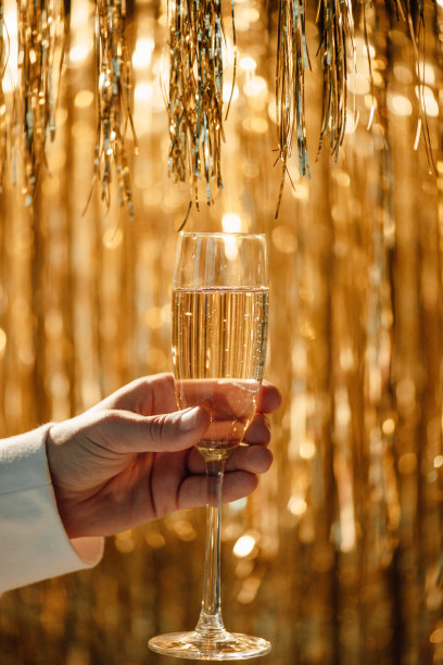 男士手中的香槟杯映衬着奢华的霞光金雨装饰奢华的假日派对图片下载