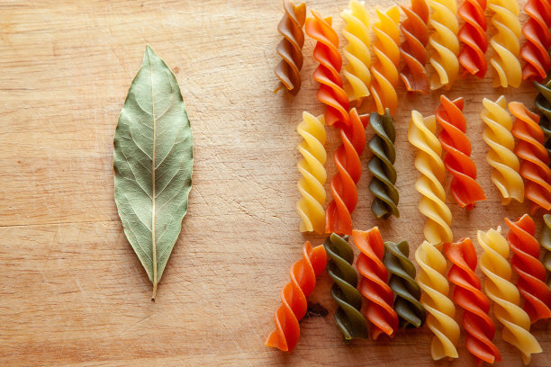 彩色意大利面和月桂叶放在木板上，俯视图。意大利小麦面食海报，日历，张贴，屏幕保护程序，封面，网站，空间为您的设计或文字。高画质照片图片下载