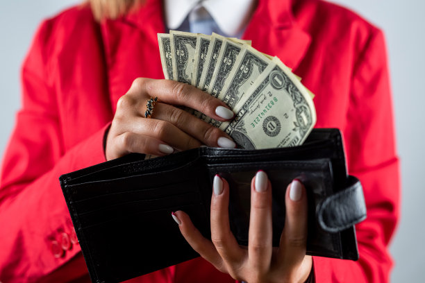一个女人美丽的手指拿着钱的特写，在她的前面有一个钱包。图片下载