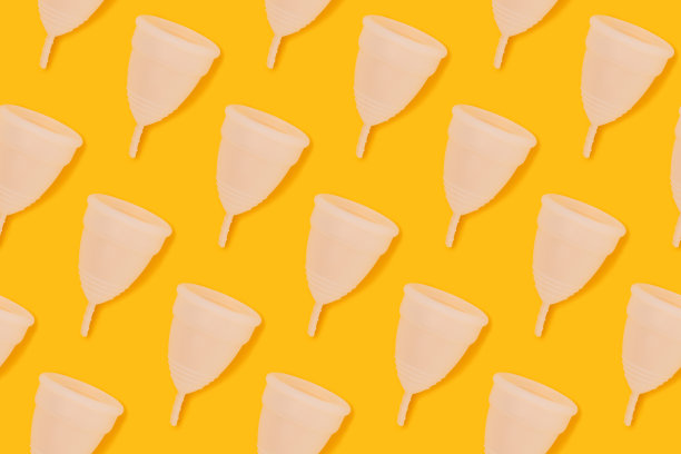 白色月经杯在黄色背景上重复的图案。图片下载