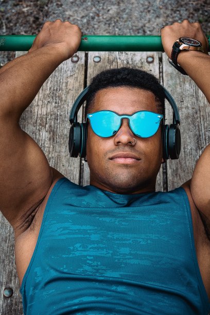 穿着蓝色衬衫，戴着墨镜的年轻健美男子一边听音乐一边在公园里锻炼图片下载