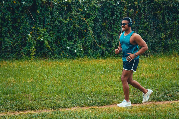 一个戴着耳机的年轻人在公园里微笑着跑步的美丽照片图片下载