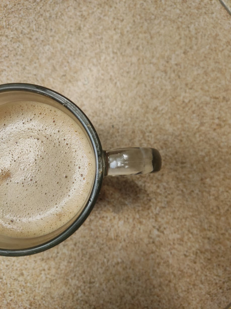 特写照片卡布奇诺咖啡在一个透明的玻璃上棕色抽象的背景。图片下载