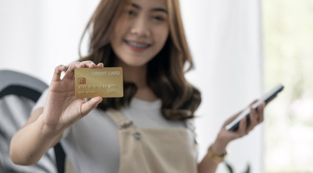 微笑的亚洲妇女展示信用卡，参与网上手机购物在家里，快乐的女性购物者购买网上商店。图片下载