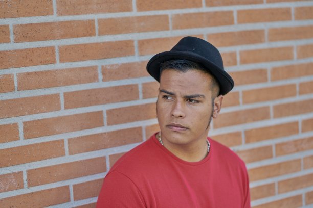 一名戴着黑色软呢帽的年轻男子站在一堵鹅卵石墙前，看上去很沮丧图片下载