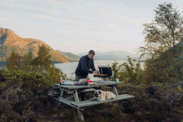 在挪威，一名男子带着一只狗在海边野餐，享受秋日图片下载
